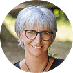 Andrea Horn vom Reisebüro Oberfell in Wolfach. Erleben Sie das bezaubernde Porträt einer strahlenden Frau, gekennzeichnet durch ihr silbernes Haar und ihre schwarz-umrandeten Brille. Dieses Bildnis ist perfekt vor dem sanften Grün des unscharfen Hintergrunds eingefangen – eine natürliche Kulisse, die es unvergesslich macht.