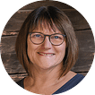 Brigitte Maier vom Reisebüro Oberfell in Zell am Harmersbach. Portrait einer lächelnden Frau mit Brille vor Holzhintergrund im Reisebüro Oberfell. - Reisebüro Oberfell, Haslach, Wolfach, Zell